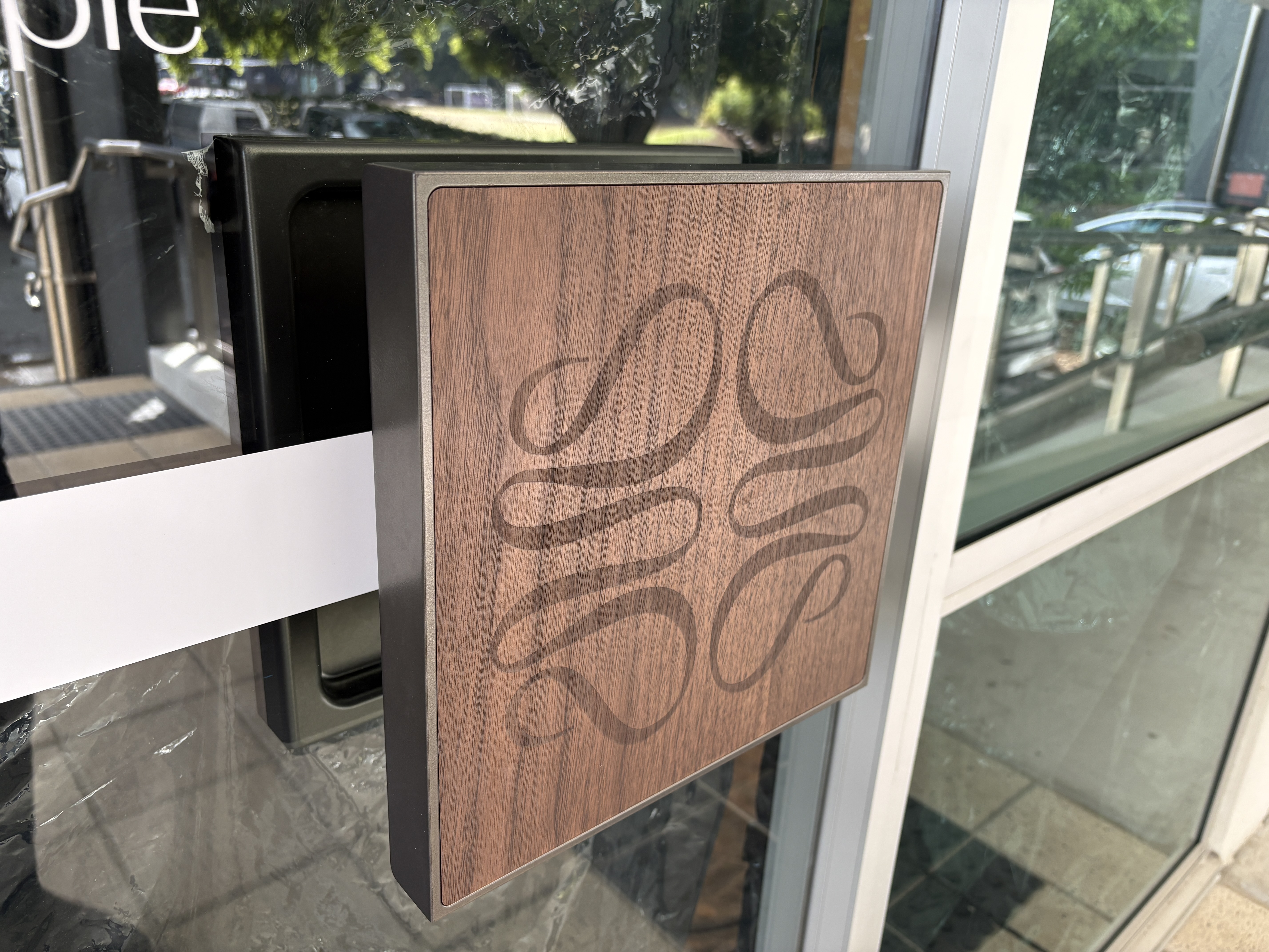 Walnut timber inlay pull with a logo etching, on a glass entry door